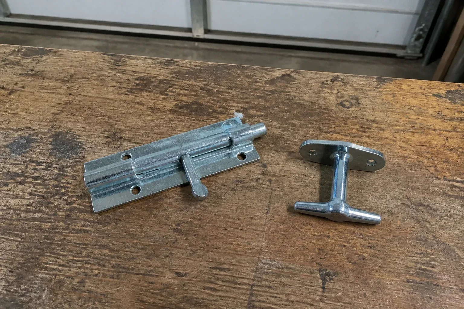 Detached slide bolt and T-handle on a wooden garage workbench. — Garage Door Manual Lock Repair, Vaughan